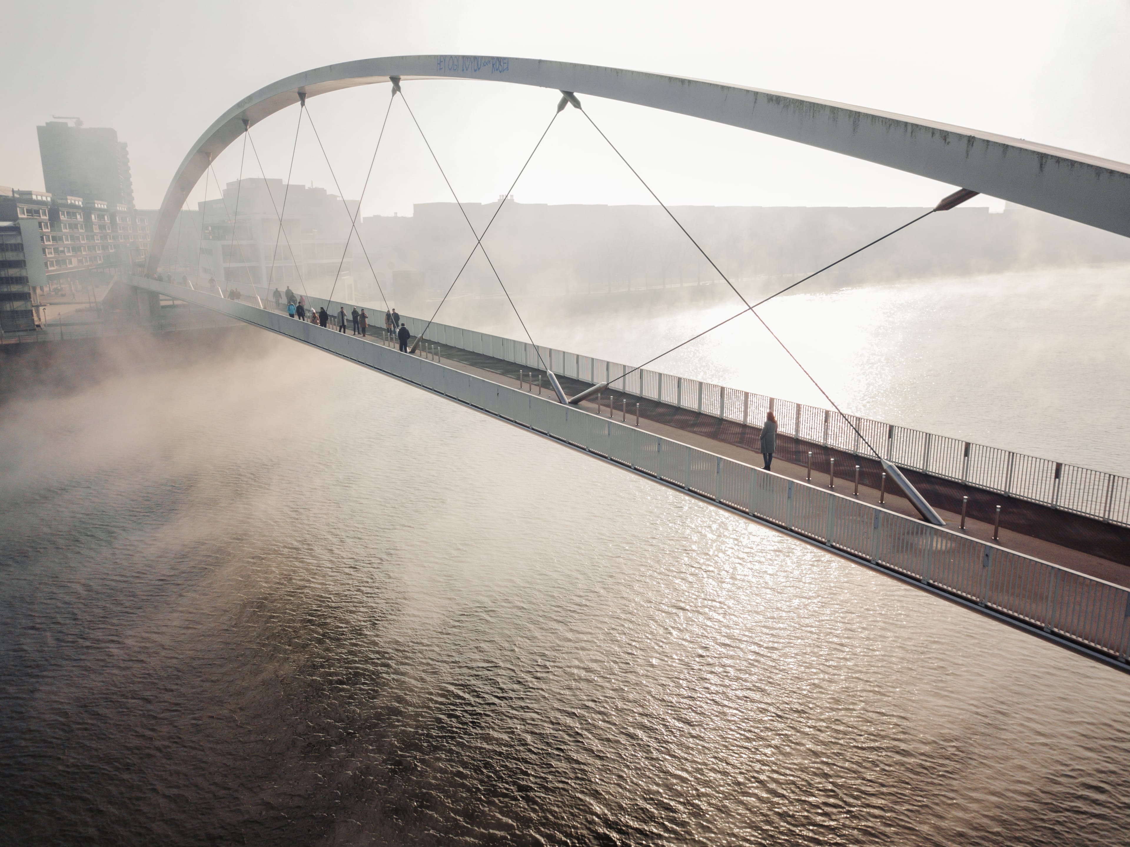 Voetgangers op een boogbrug over het water in de ochtendmist